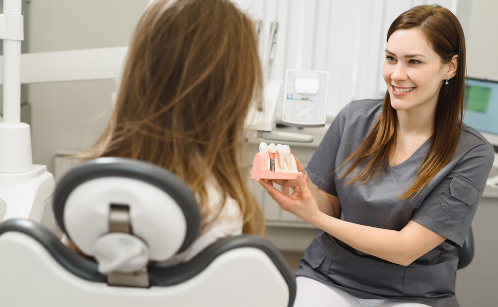 dental assistant showing patient a mode of a dental implant